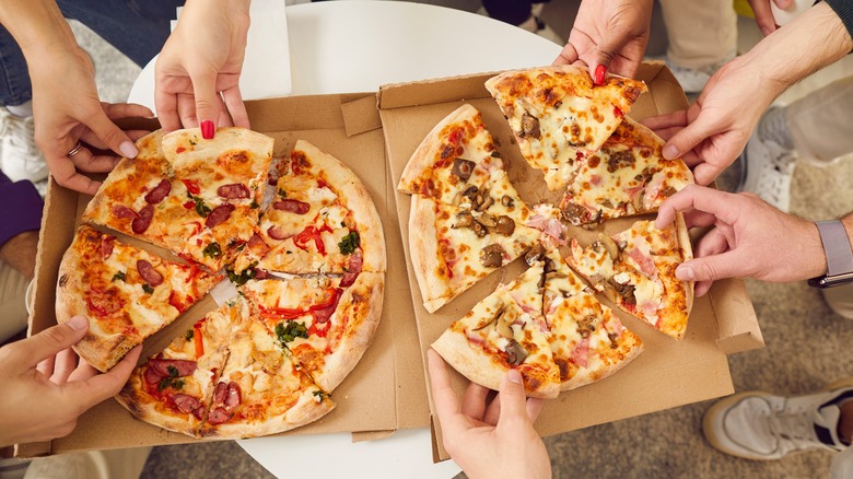 People grabbing slices of pizza from box