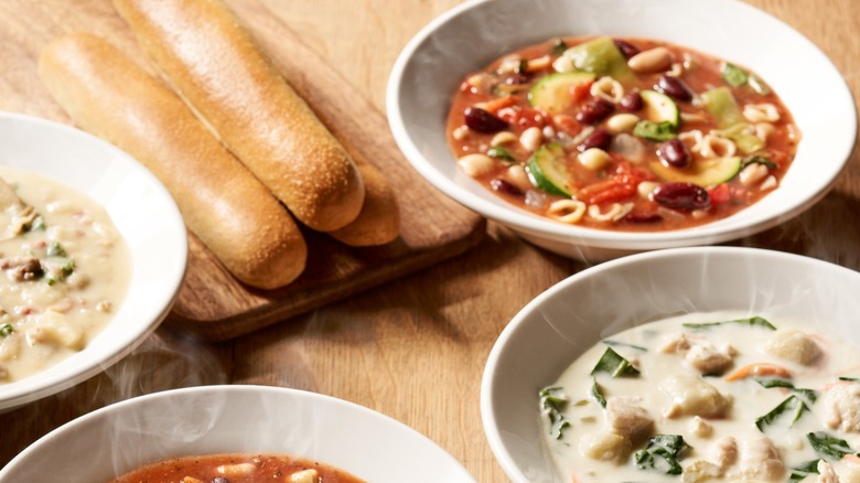 Four bowls of Olive Garden soup and breadsticks