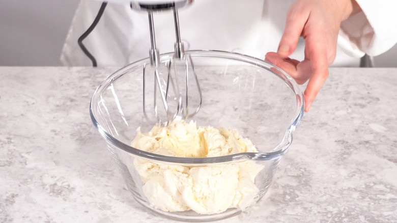 A hand working with a clear bowl of white vanilla frosting.