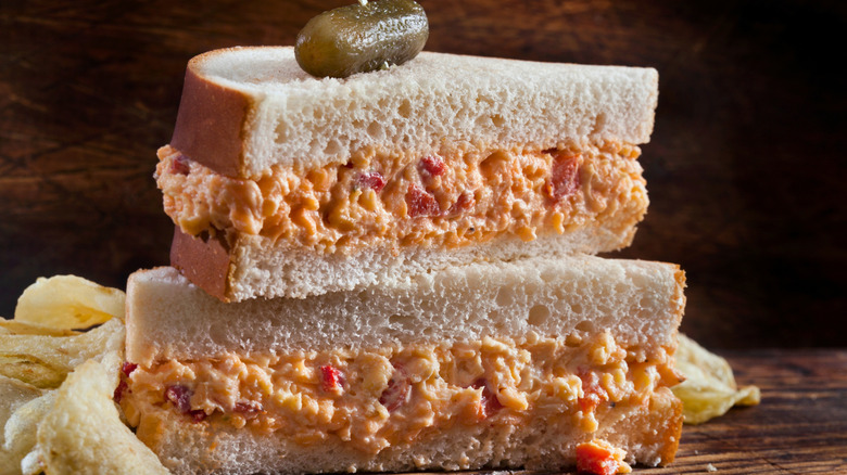 Pimento cheese sandwich cut in half and stacked, topped with a pickle