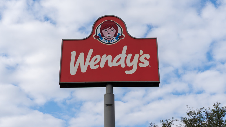 Close up of a Wendy's sign in front of a partly cloudy sky