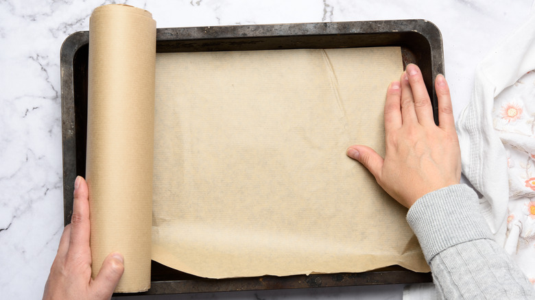 A person covering a baking sheet with parchment paper