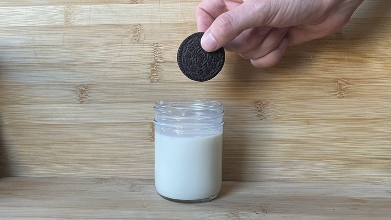 A hand holds an Oreo over a glass of milk.