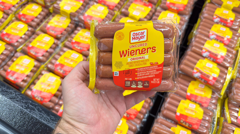 A person holding a pack of Oscar Mayer wieners in front of a store display