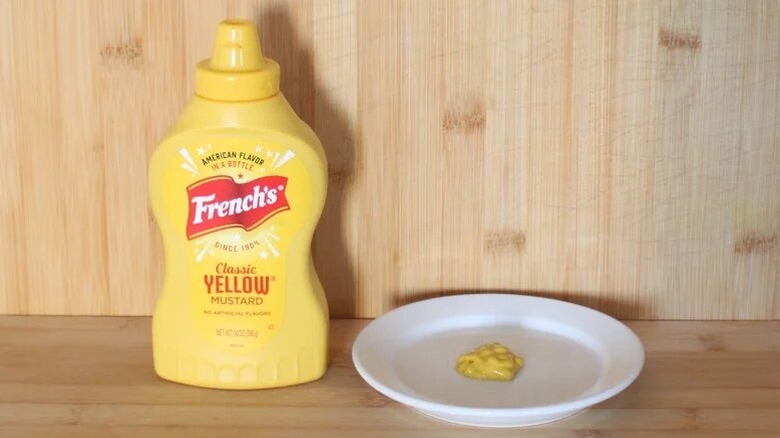 A bottle of French's yellow mustard, with a dab on a white plate.