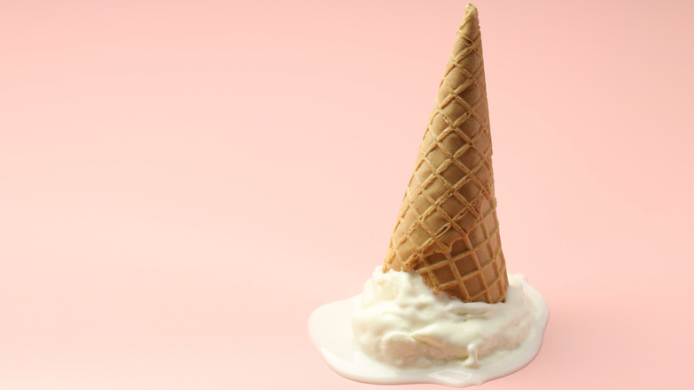 Upside down ice cream cone with melted vanilla ice cream underneath against light pink background