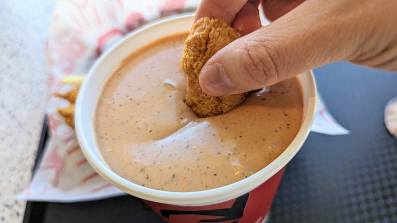 hand dipping tender in cup of sauce