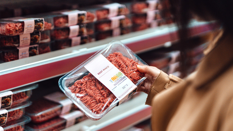 A woman holding a package of beef mince (ground beef) inside a grocery store