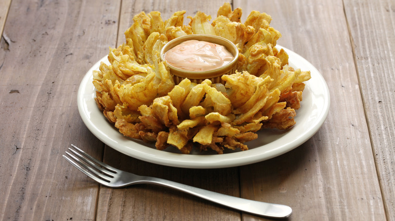 Blooming onion appetizer on white plate with dip in center