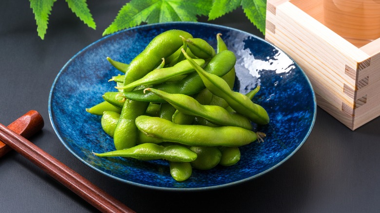 Edamame on blue plate by leaves and chopsticks