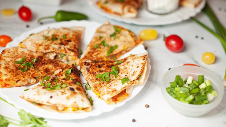 Quesadillas fanned out on white plate with green onions