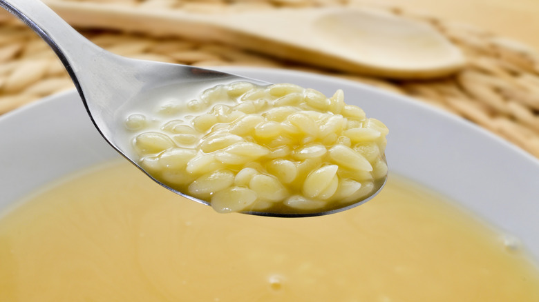 Close-up of pastina on a spoon with a bowl of broth in the background