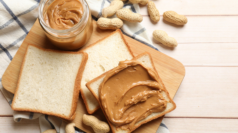 Peanut butter on bread next to a tub and peanuts