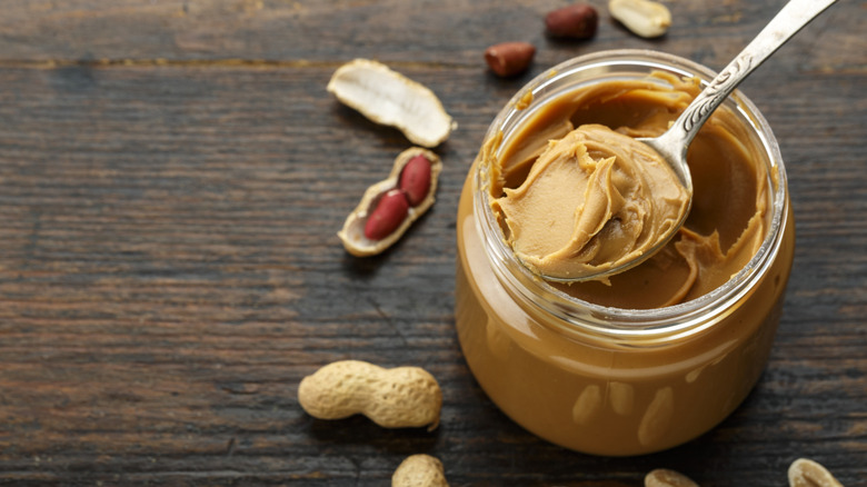 Open jar of peanut butter with peanuts on wooden table