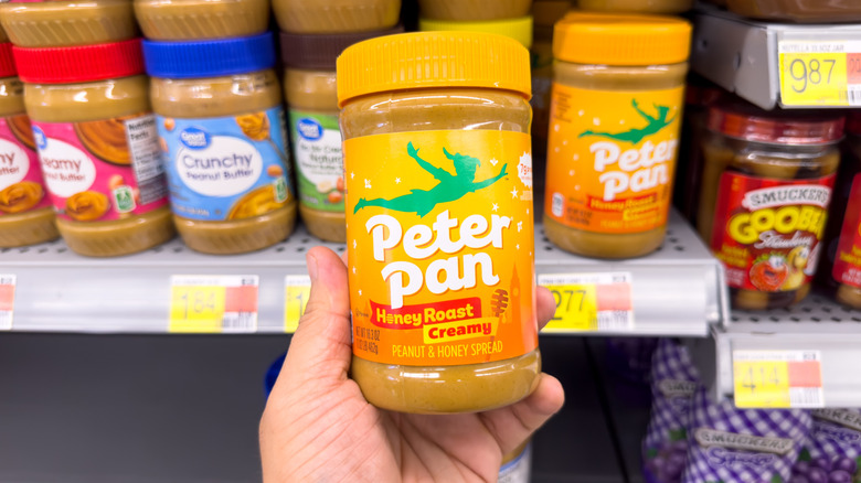 Hand holding jar of Peter Pan peanut butter in grocery store