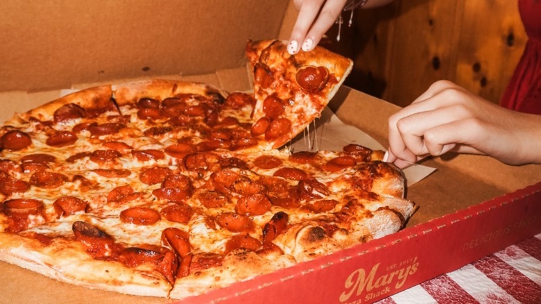 Hand pulling pizza slice from Mary's Pizza Shack box