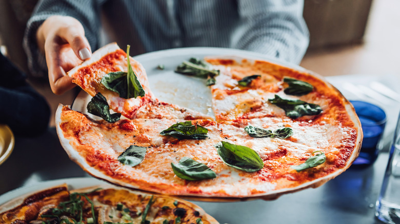 Person taking slice of Margherita pizza