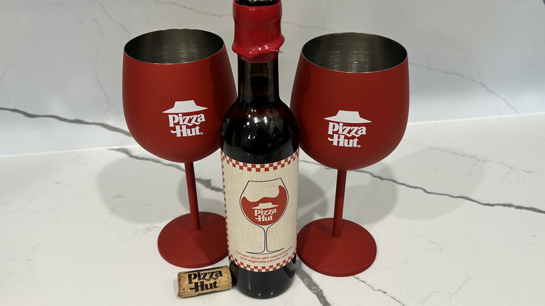 Two Pizza Hut branded wine glasses sit on a counter with a bottle of Pizza Hut wine