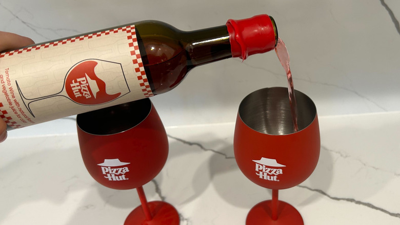 A bottle of tomato wine is poured in a Pizza Hut wine glass