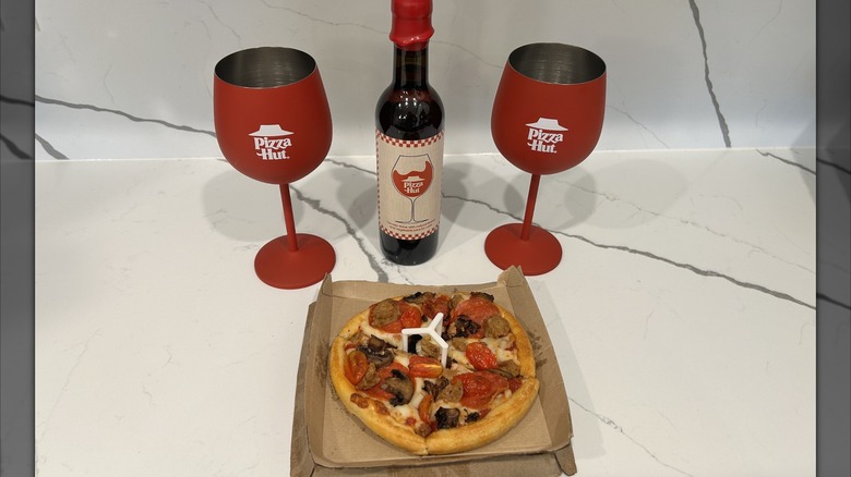 Two Pizza Hut branded glasses, a Pizza Hut wine bottle, and a Pizza Hut personal pan pizza sit on a counter