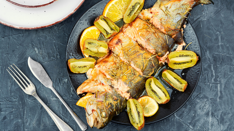 Cooked whole trout on a plate with kiwi and oranges