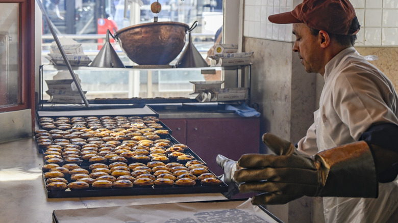 A baker taking out of the oven trays with pasteis de nata.