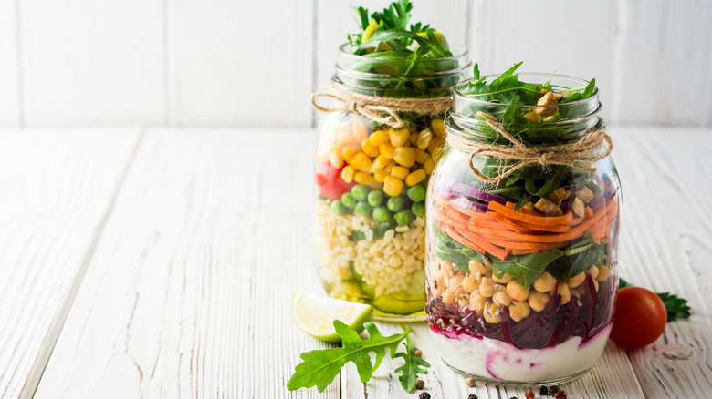 Two mason jar meals with layers of different fresh produce