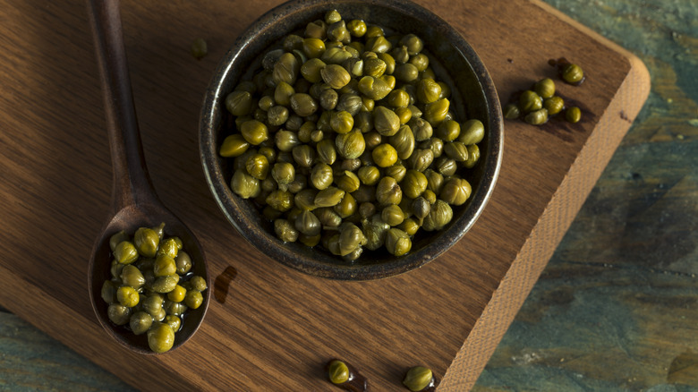 Marinated caper berries in a bowl and spoon on a wooden board