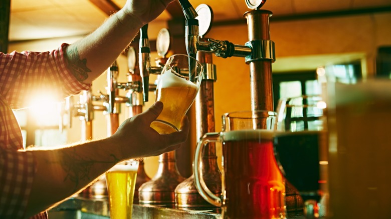 Person pouring a beer out of a tap while other types of beer sit nearby