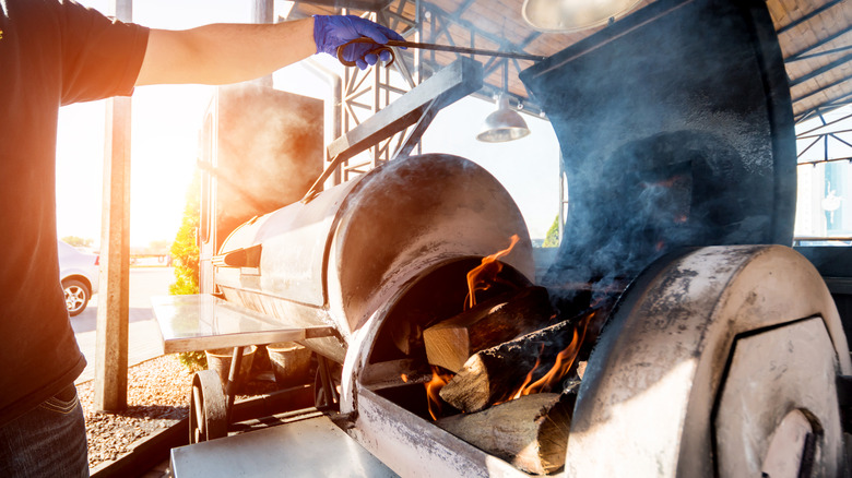 person opening meat smoker with wood on fire