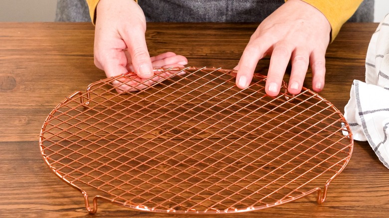 A person using a wire cooling rack on a wooden surface