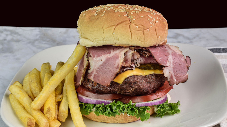 Pastrami-topped cheeseburger on a plate with fries