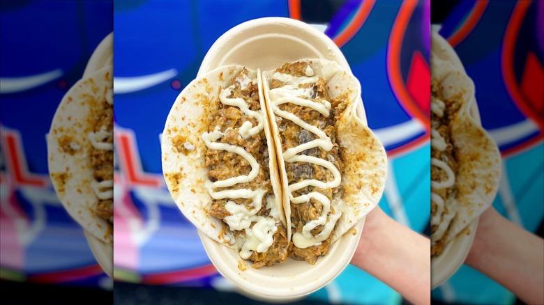 Hand holding bowl containing two cheesesteak tacos