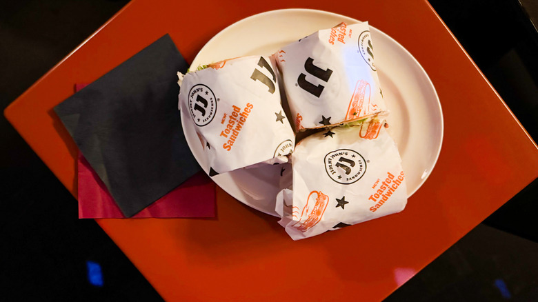 A trio of Jimmy John's toasted sandwiches on a white plate on a red table