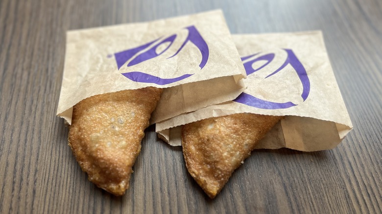 two Caramel Apple Empanada in paper sleeves, sitting on a table