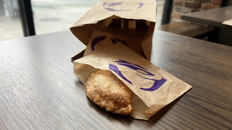 a Taco Bell bag with a Caramel Apple Empanada falling out of it