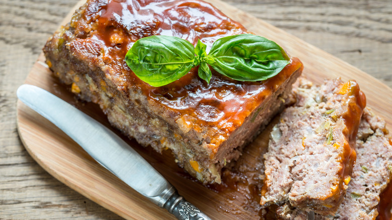 meatloaf with glaze and a green garnish on it partially sliced by a knife