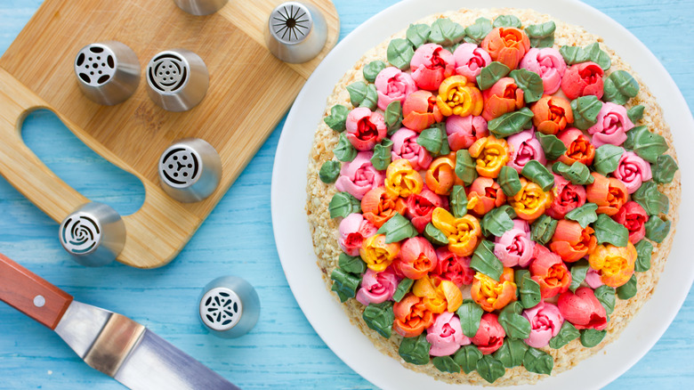 cake frosted with flowers on white plate with russian piping tips beside it