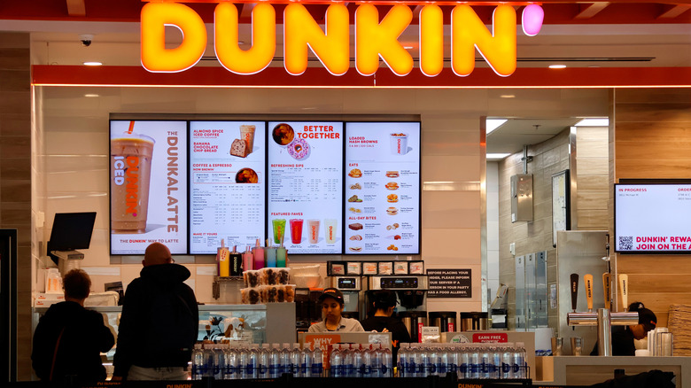 A Dunkin' menu hangs over the storefront counter as people order