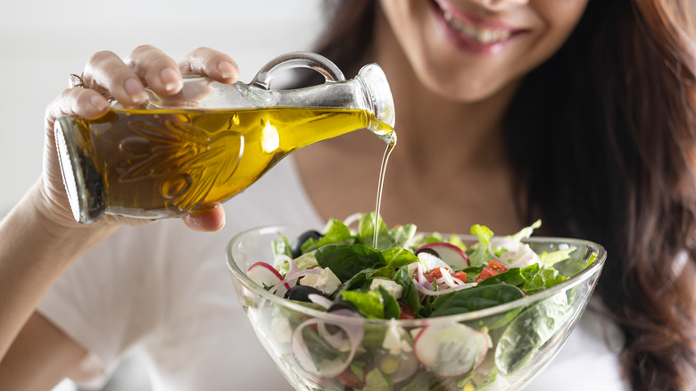 woman pouring oil out of a glass bottle into her salad