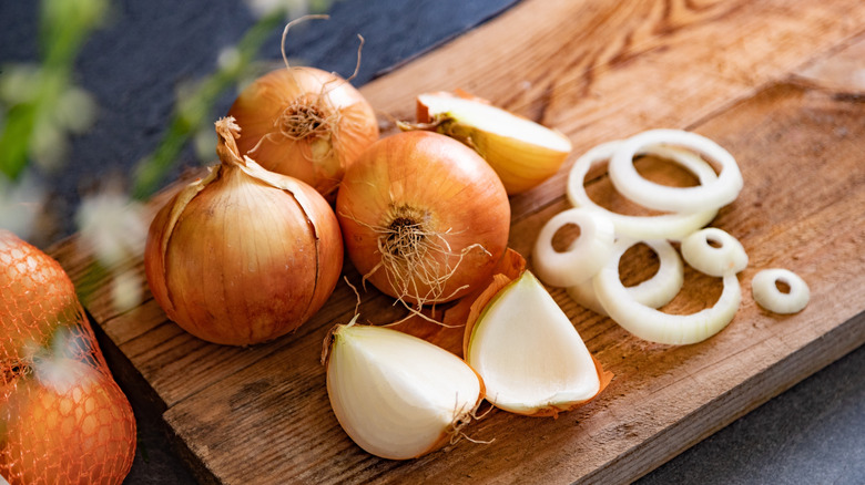 Whole yellow onions next to sliced onions on a cutting board