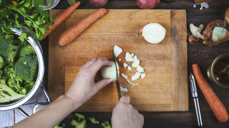 Person cutting an onion on a cutting board with carrots and broccoli nearby