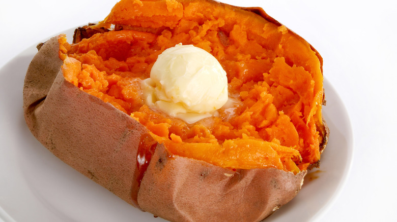 A baked sweet potato topped with melting butter on a white plate