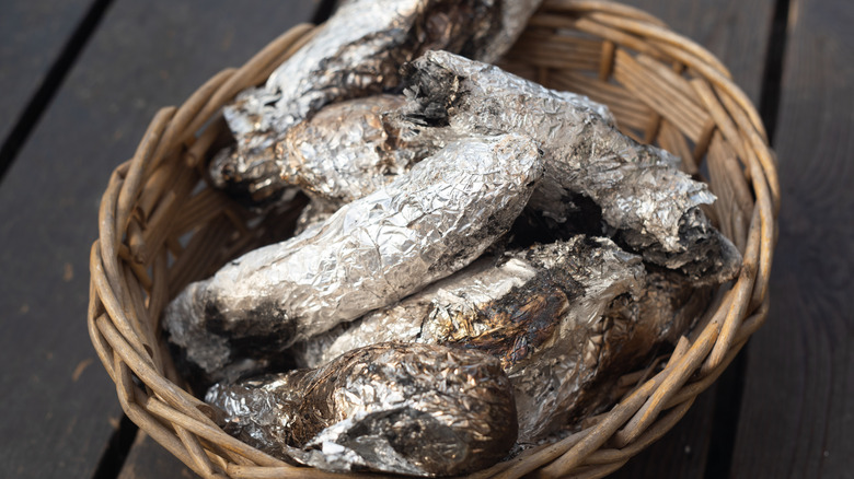 A woven basket containing a pile of tin foil-wrapped sweet potatoes