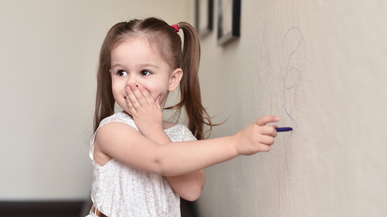 little girl scribbling with crayon on a wall