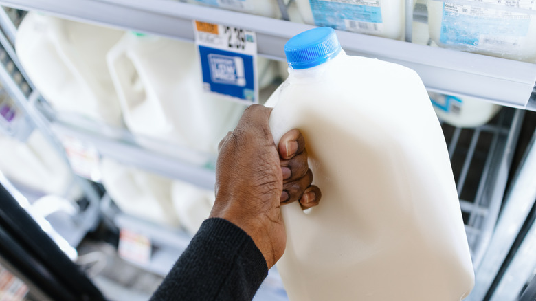 hand grabbing milk gallon from dairy case