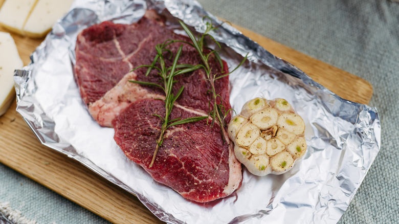 raw steak and garlic on aluminum foil before being cooked