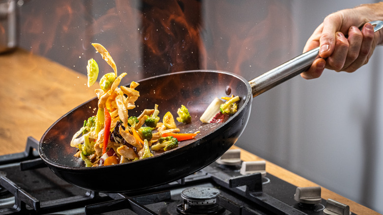 Person flipping stir fry in a pan over a gas stove