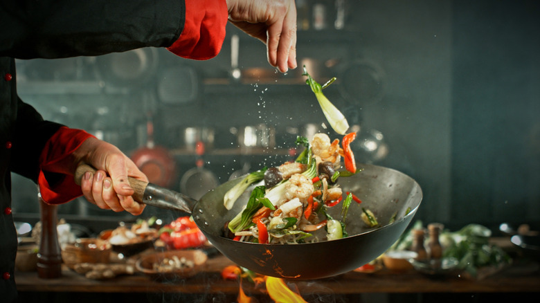 Chef sprinkling salt over a stir fry medley in a pan