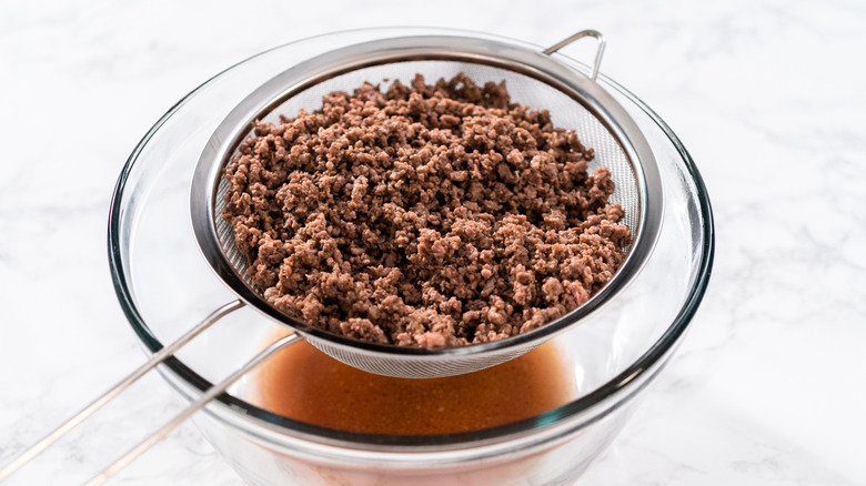 Ground beef draining in a sieve above a glass bowl